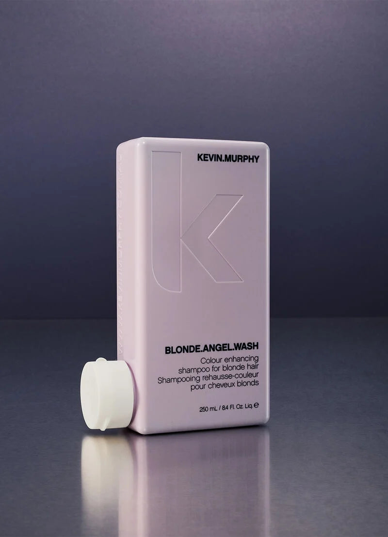 Kevin Murphy Blonde Angel Wash shampoo bottle in a pale lavender-pink color, shown with its white cap off on a dark reflective surface against a dark gray background.