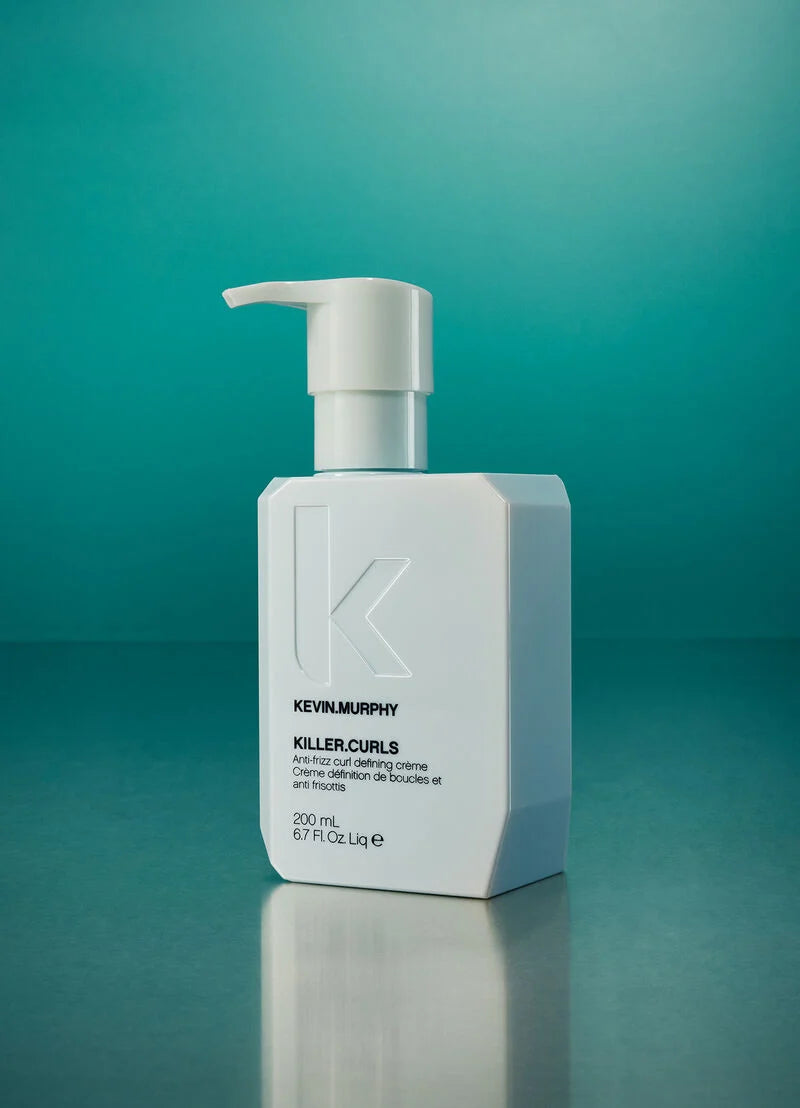 A white rectangular pump bottle of Kevin Murphy Killercurls Cleansing Cream with a large embossed 'K' logo, set against a teal gradient background with a soft reflection below.