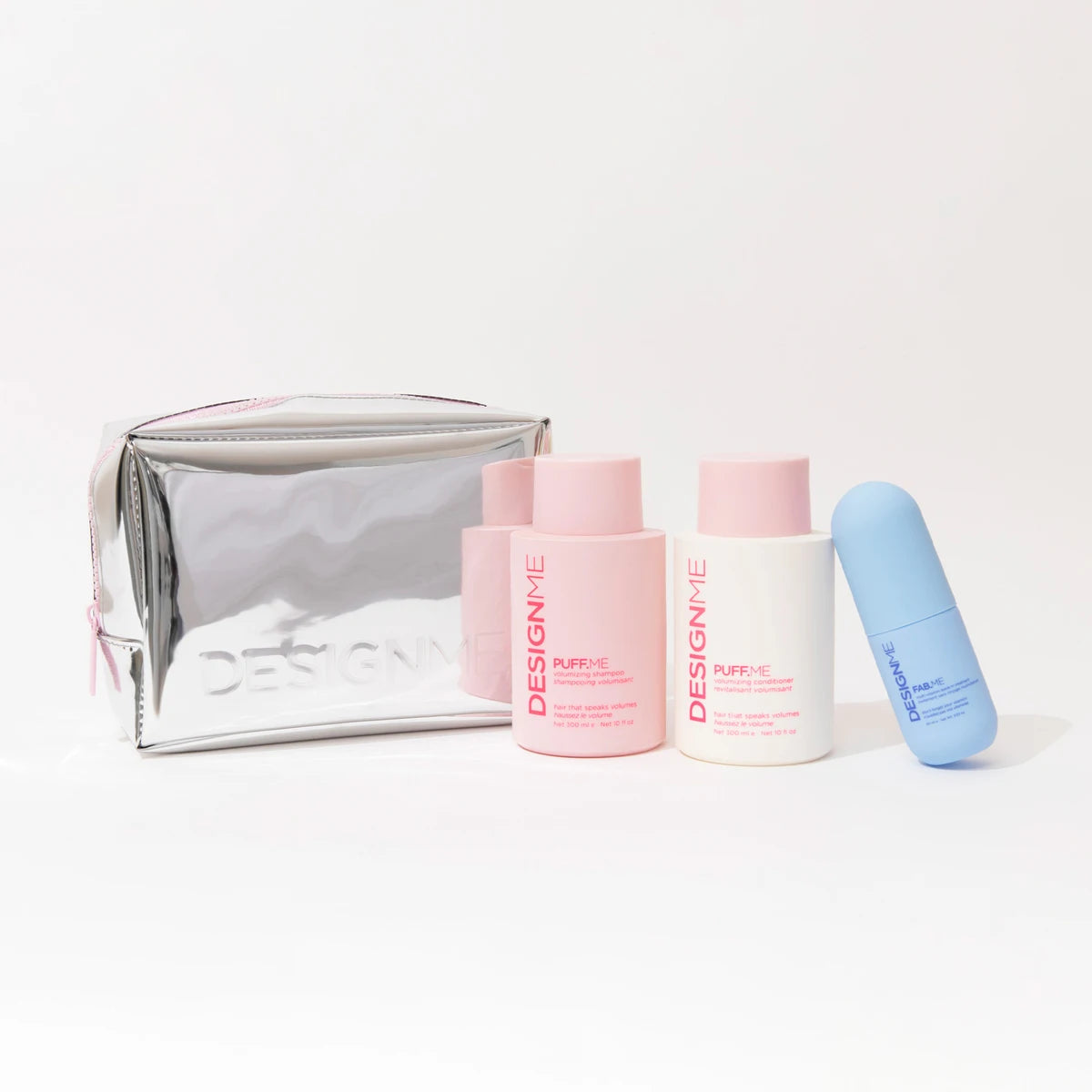 A skincare gift set featuring a metallic silver zippered pouch, two pink bottles, one white bottle, and one blue tube from the brand DesignMe, arranged on a clean white background.
