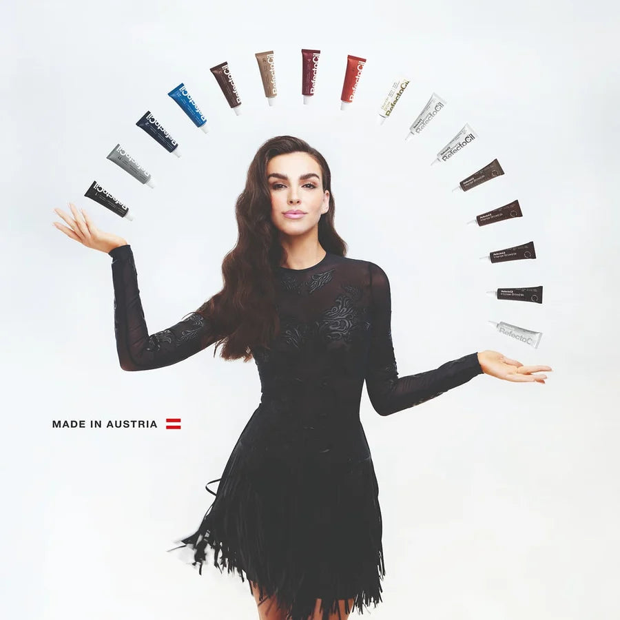 A woman in a black long-sleeve dress stands against a white background with her arms outstretched, surrounded by a semi-circle of cosmetic tubes in various colors. Text at the bottom left reads 'MADE IN AUSTRIA' with an Austrian flag.