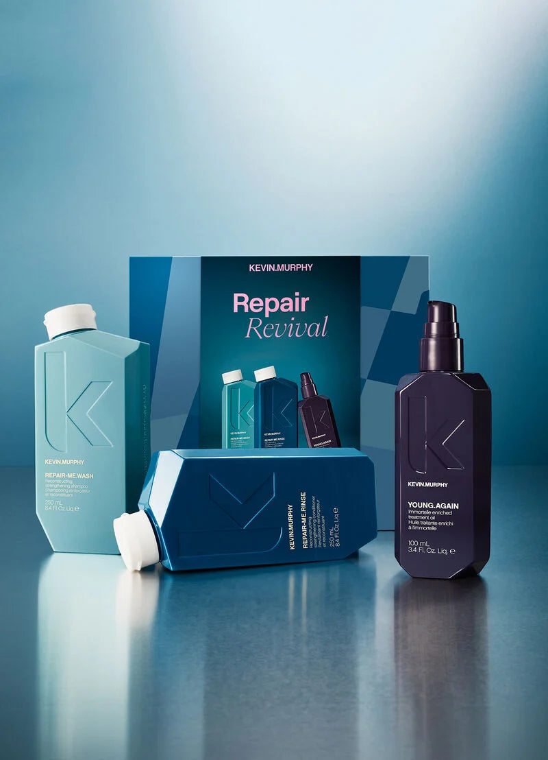 Kevin Murphy Repair Revival haircare set featuring a large teal bottle, a dark purple spray bottle, and blue packaging boxes on a reflective blue surface.
