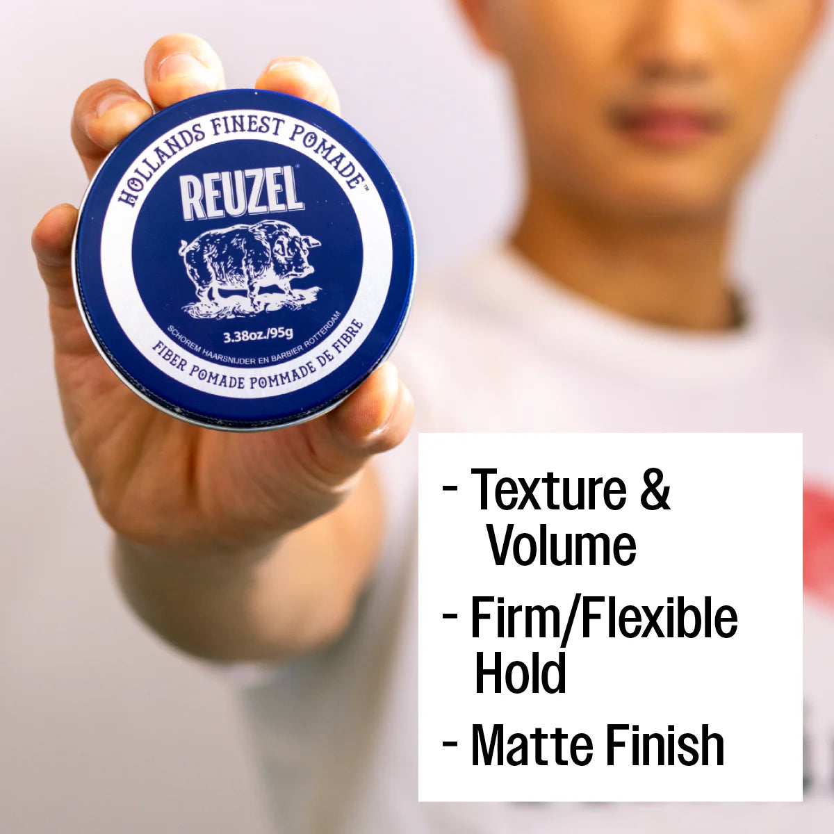 Hand holding a Reuzel pomade container with product features displayed.