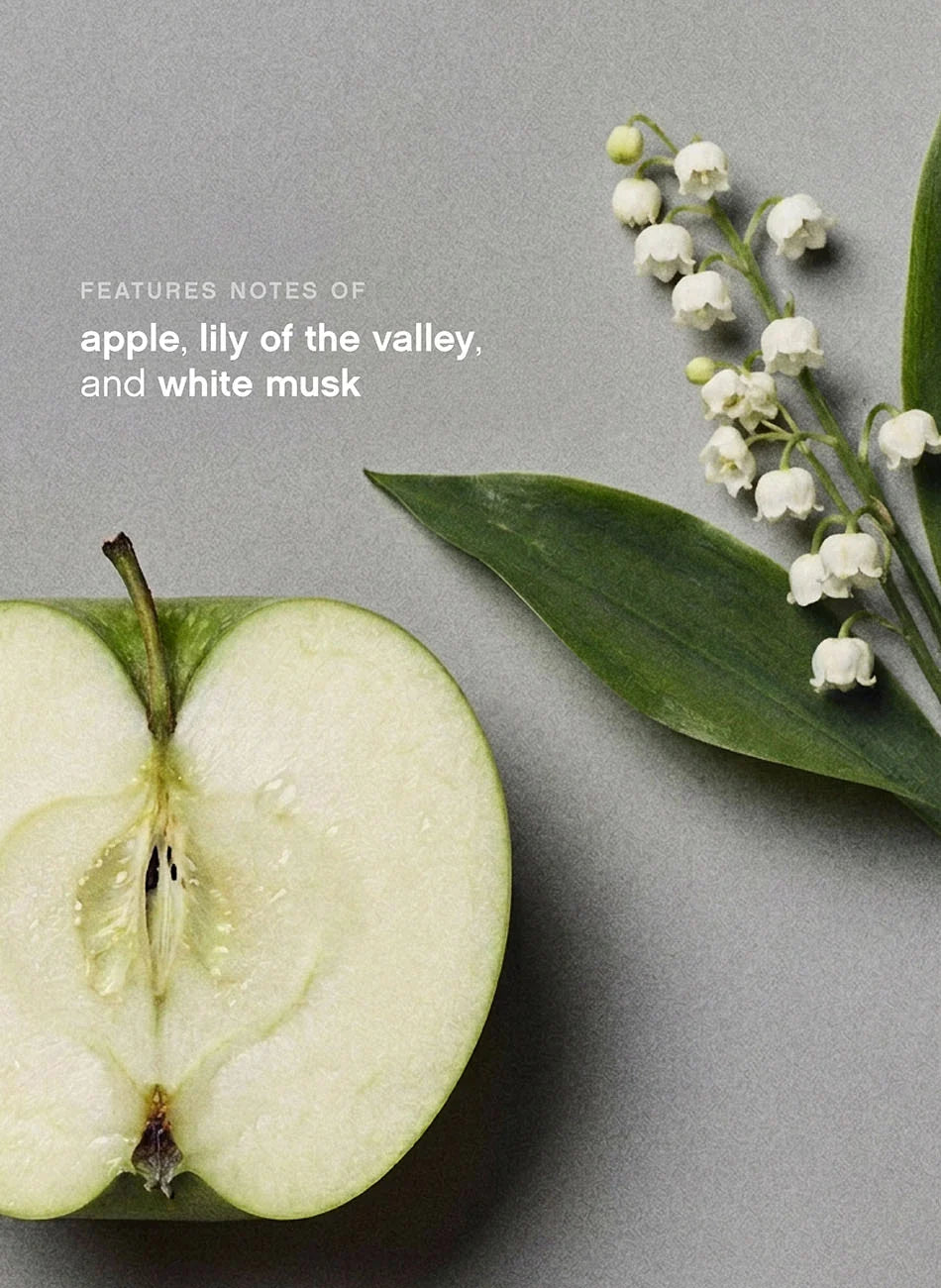A styled flat-lay featuring a halved green apple, white lily of the valley flowers with green stems, and white text reading 'FEATURES NOTES OF apple, lily of the valley, and white musk' on a soft gray background.