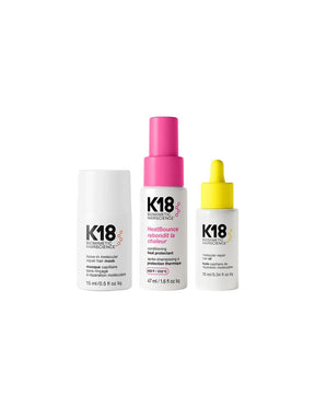 Three K18 haircare products on a white background: a white bottle with black text, a white bottle with a bright pink spray top, and a white dropper bottle with a yellow cap.