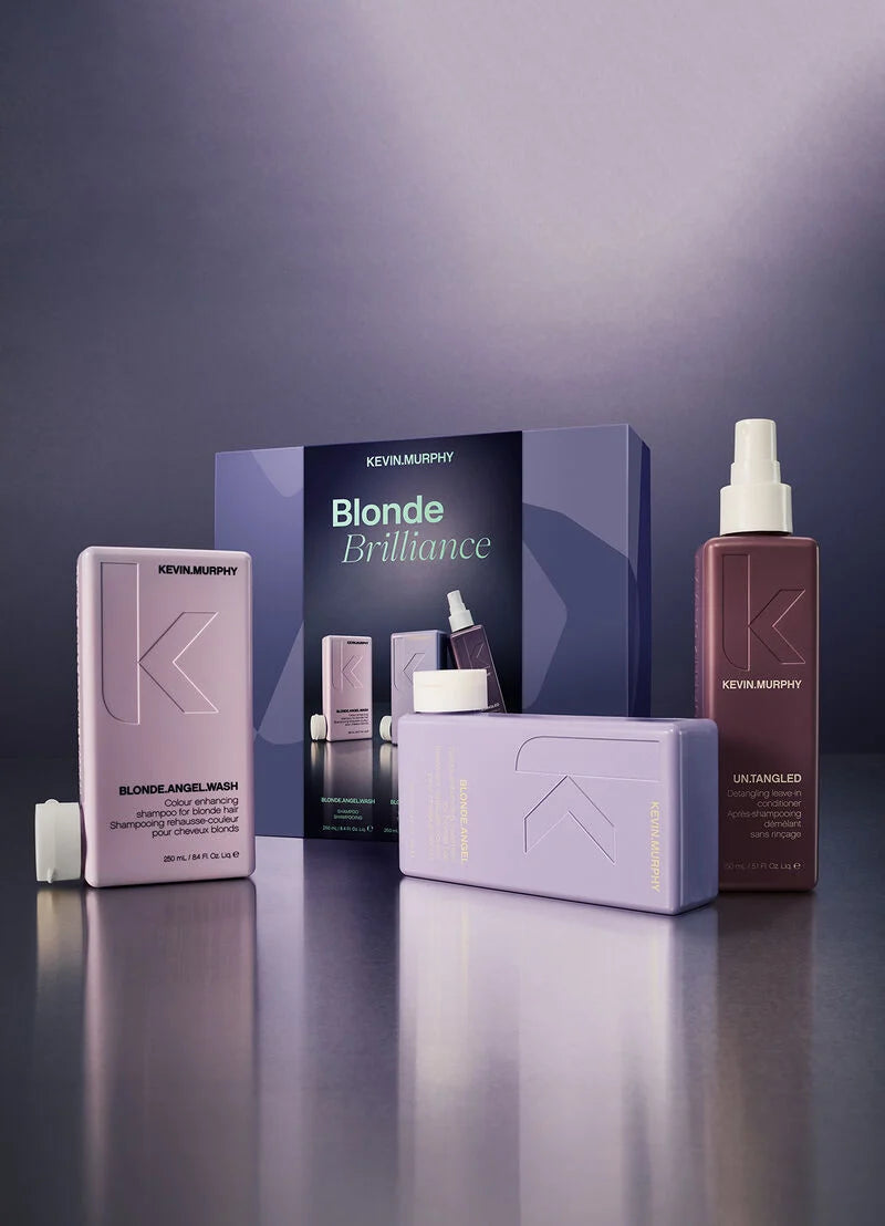 Kevin Murphy Blonde Brilliance haircare set featuring a lavender Angel Wash bottle, a mauve Unbleached bottle with spray, and a dark blue product box, arranged on a reflective dark surface.