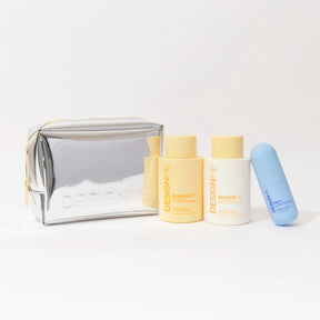A silver metallic cosmetic pouch with gold zipper and trim sits next to three DesignMe skincare bottles and a blue lip balm tube on a clean white background.