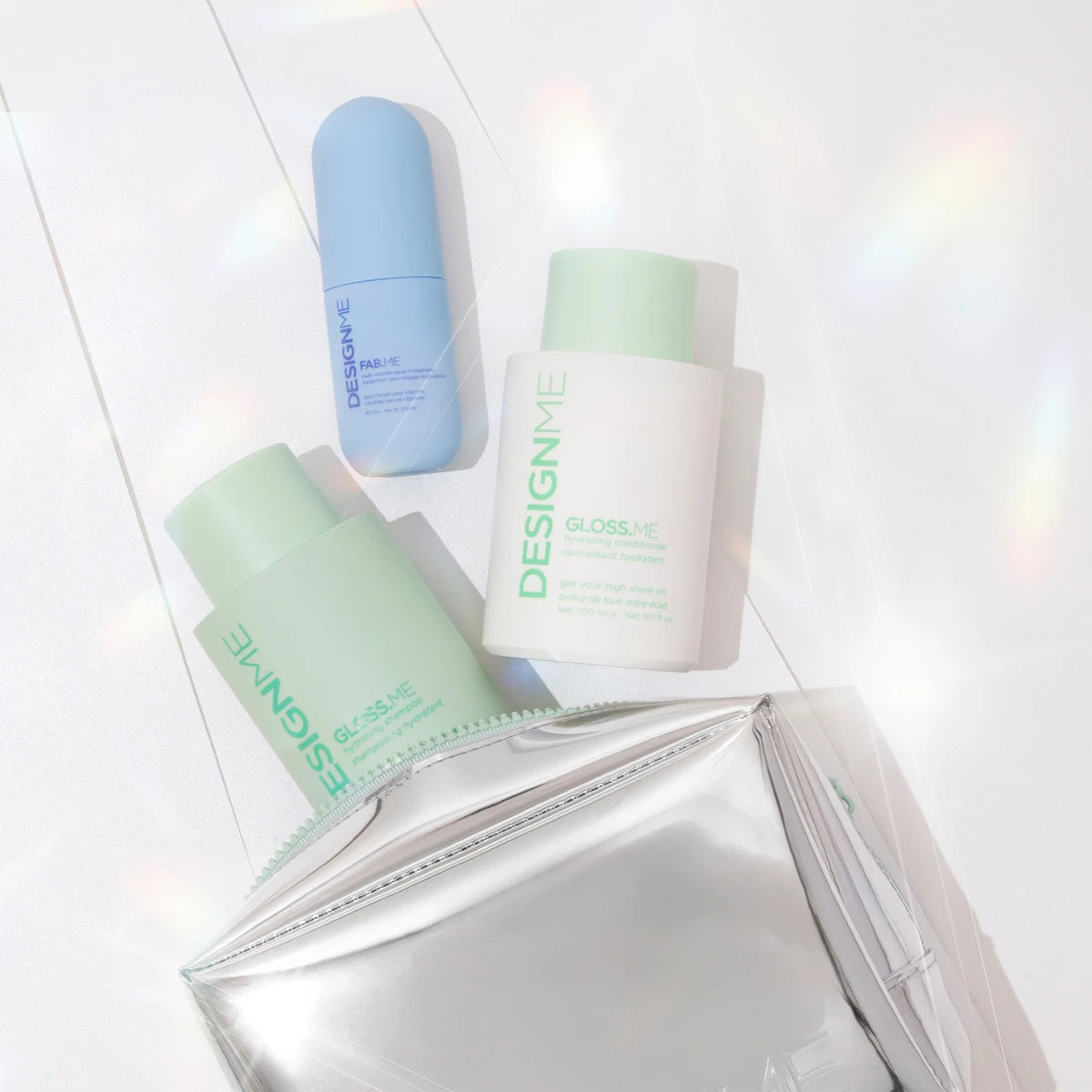 Three DESIGN ME cosmetic bottles in pastel blue, mint green, and white, arranged with a metallic silver pouch on a glossy white surface with soft rainbow light leaks.
