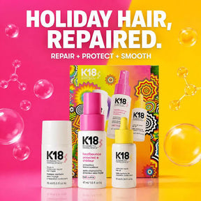 K18 Hair Sciences Holiday Hair, Repair set featuring three hair care bottles (conditioner, repair spray, and smoothing treatment) arranged in front of a colorful patterned box on a vibrant pink and yellow split background with floating bubbles.