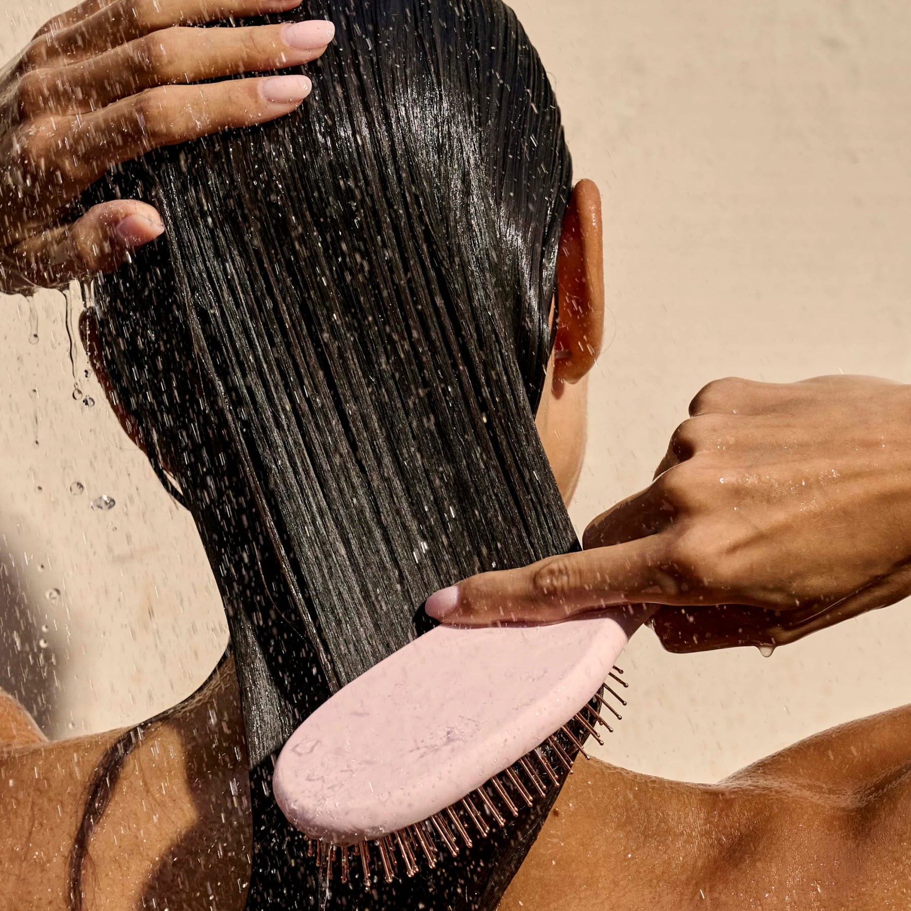 Person brushing wet hair with a pink brush against a neutral background