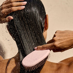 Person brushing wet hair with a pink brush against a neutral background