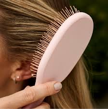 Person holding a pink hairbrush with bristles against their hair
