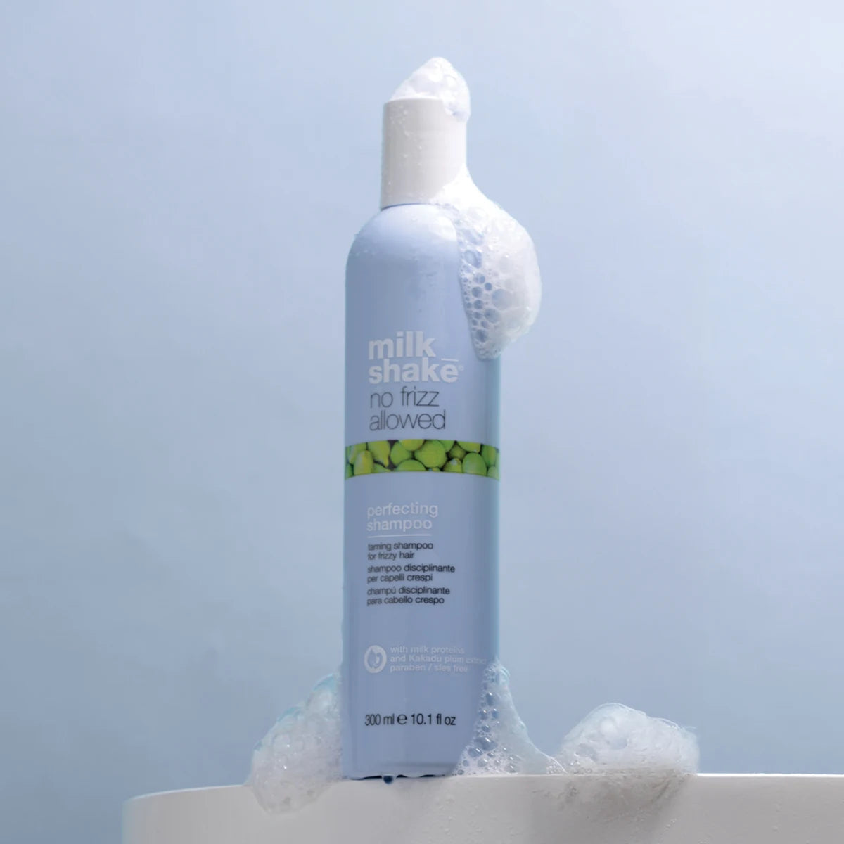 Bottle of 'milk shake no frizz allowed' shampoo with bubbles on a light blue background