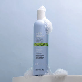 Bottle of 'milk shake no frizz allowed' shampoo with bubbles on a light blue background