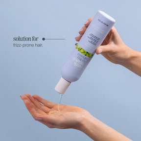 Hand holding a bottle of hair care product with a blue background