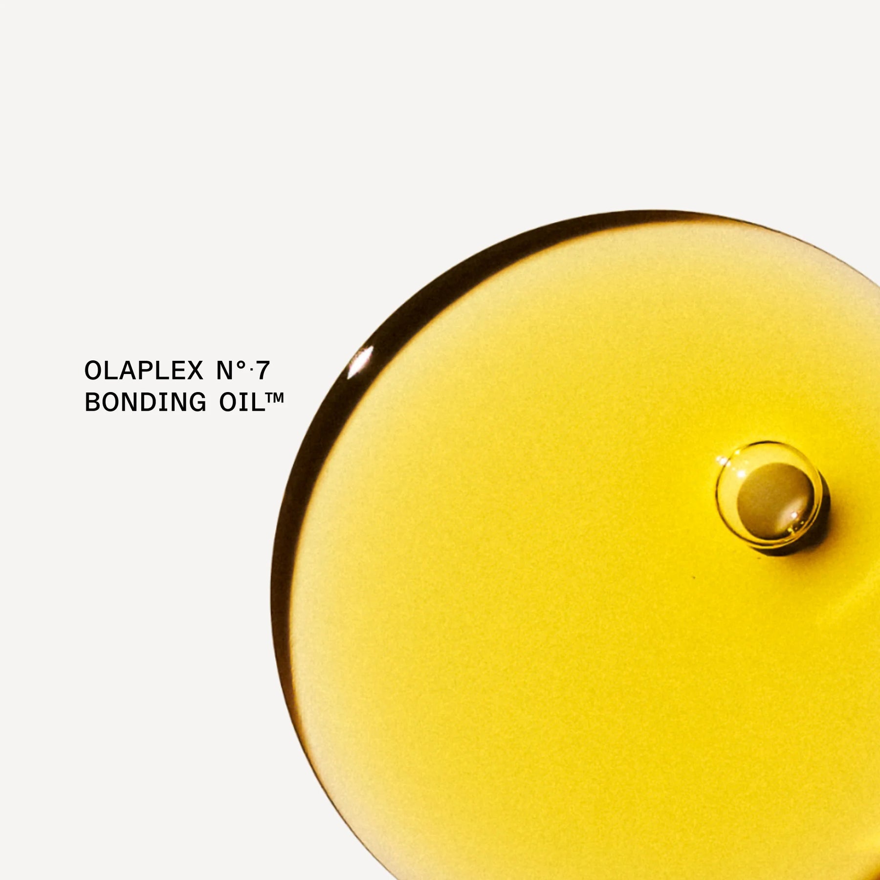 A close-up studio shot of a glossy, translucent droplet of yellow-gold liquid on a white background, with the text 'OLAPLEX N°7 BONDING OIL' visible on the left.