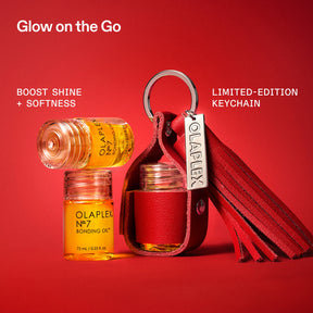 A red leather keychain pouch with a silver metal ring and a branded Olaplex tag, shown alongside two small amber bottles of Olaplex No. 7 Bonding Oil on a solid red background.