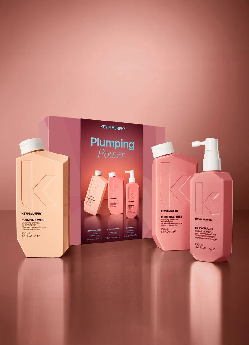 Kevin Murphy Plumping Power hair care set featuring a peach-colored shampoo bottle, a pink body wash bottle, and a pink body mass bottle arranged in front of a matching product box on a reflective dusty rose surface.