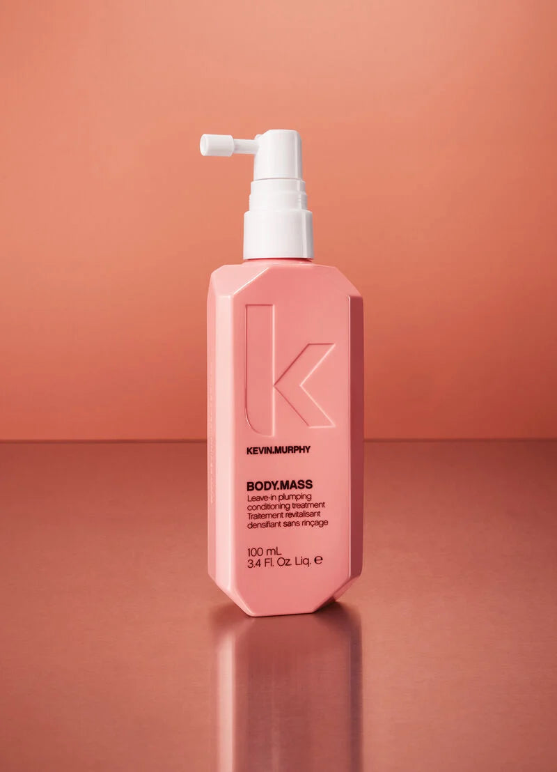 A bottle of Kevin Murphy Body Mass Use-in-plumping conditioning treatment, in a faceted pink bottle with a white pump dispenser, set against a matching pink background.