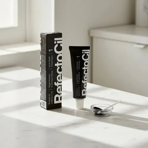 A black tube and matching box of RefectoSil eyelash and eyebrow enhancer sit on a white marble countertop with a small glass dish and applicator in a bright, sunlit room.