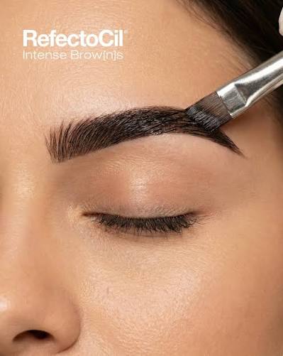Close-up of a person's eyebrow being filled in with a dark brown cosmetic product using a brush. The text 'RefectoCil Intense BrowJs' is visible in the upper left corner.
