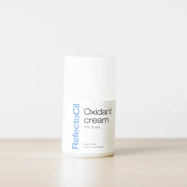 A white cylindrical bottle of RefectoCil Oxidant cream 3% 10vol, standing on a light wooden surface against a clean white background.