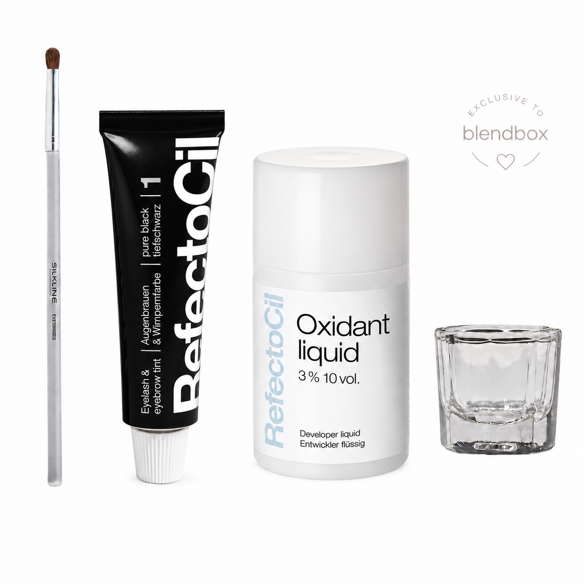 A beauty product set on a white background featuring a black tube of RefectoSil black eyeliner, a white bottle of RefectoSil oxidant liquid, a clear glass mixing cup, and a clear makeup brush with brown bristles. A 'EXCLUSIVE TO blendbox' badge is visible in the top right.