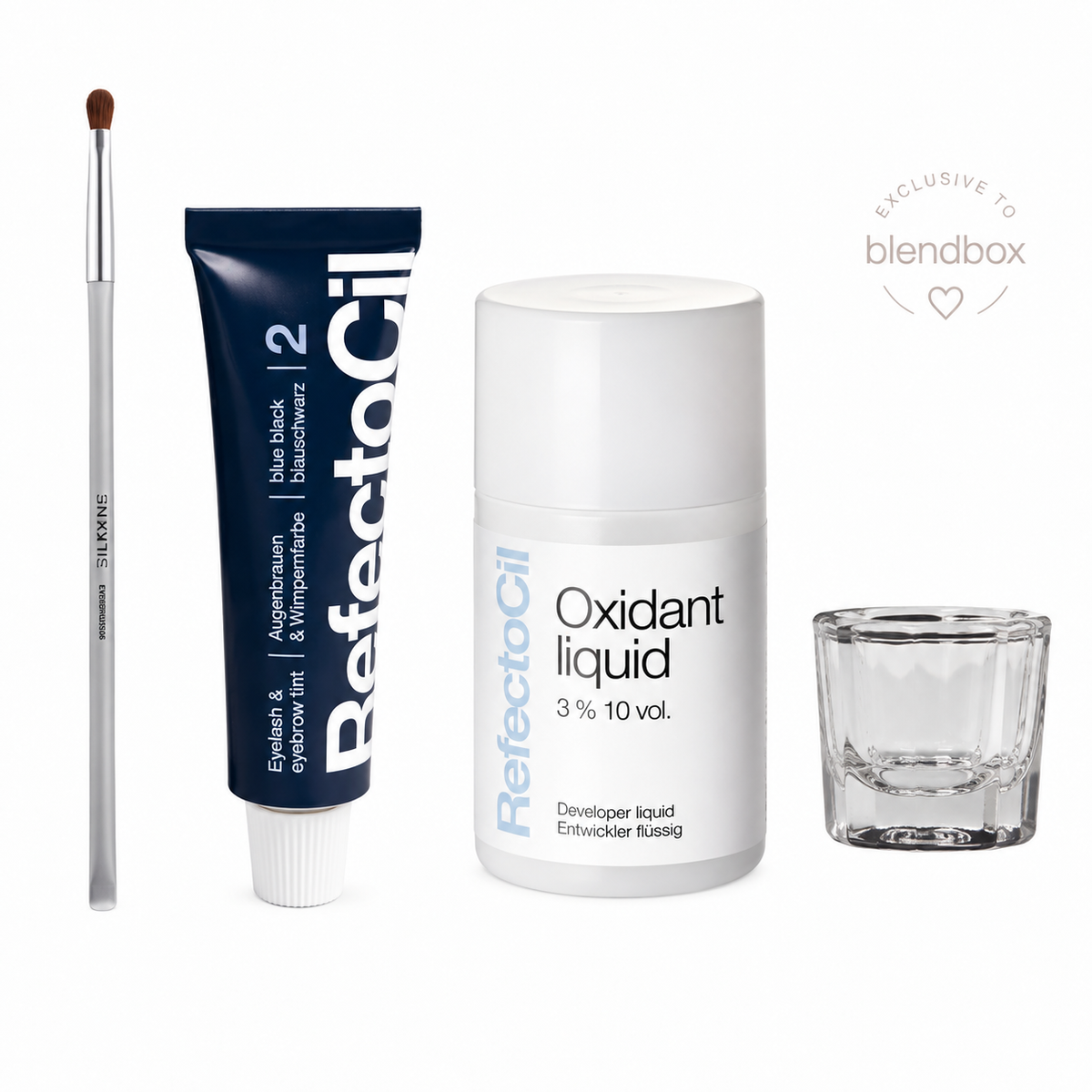 A beauty product set on a white background, including a blue and white tube of RefectoSil 2 Blue Black Eyeshadow, a white bottle of RefectoSil 3% 10 vol. Oxidant liquid, a small clear glass mixing cup, and a makeup brush.
