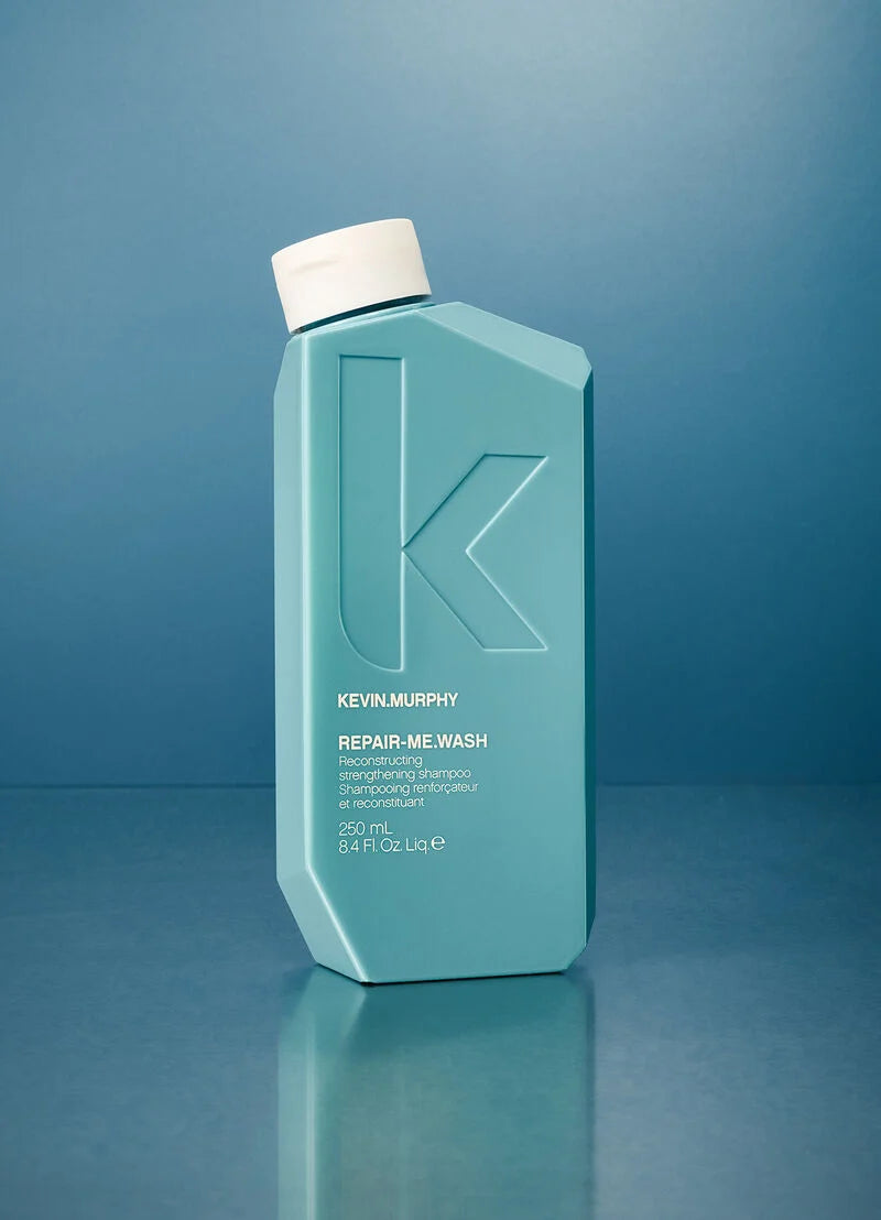 A 250 mL bottle of Kevin Murphy Repair-Me Wash in a light teal color with a white cap, standing on a reflective blue surface against a matching blue background.
