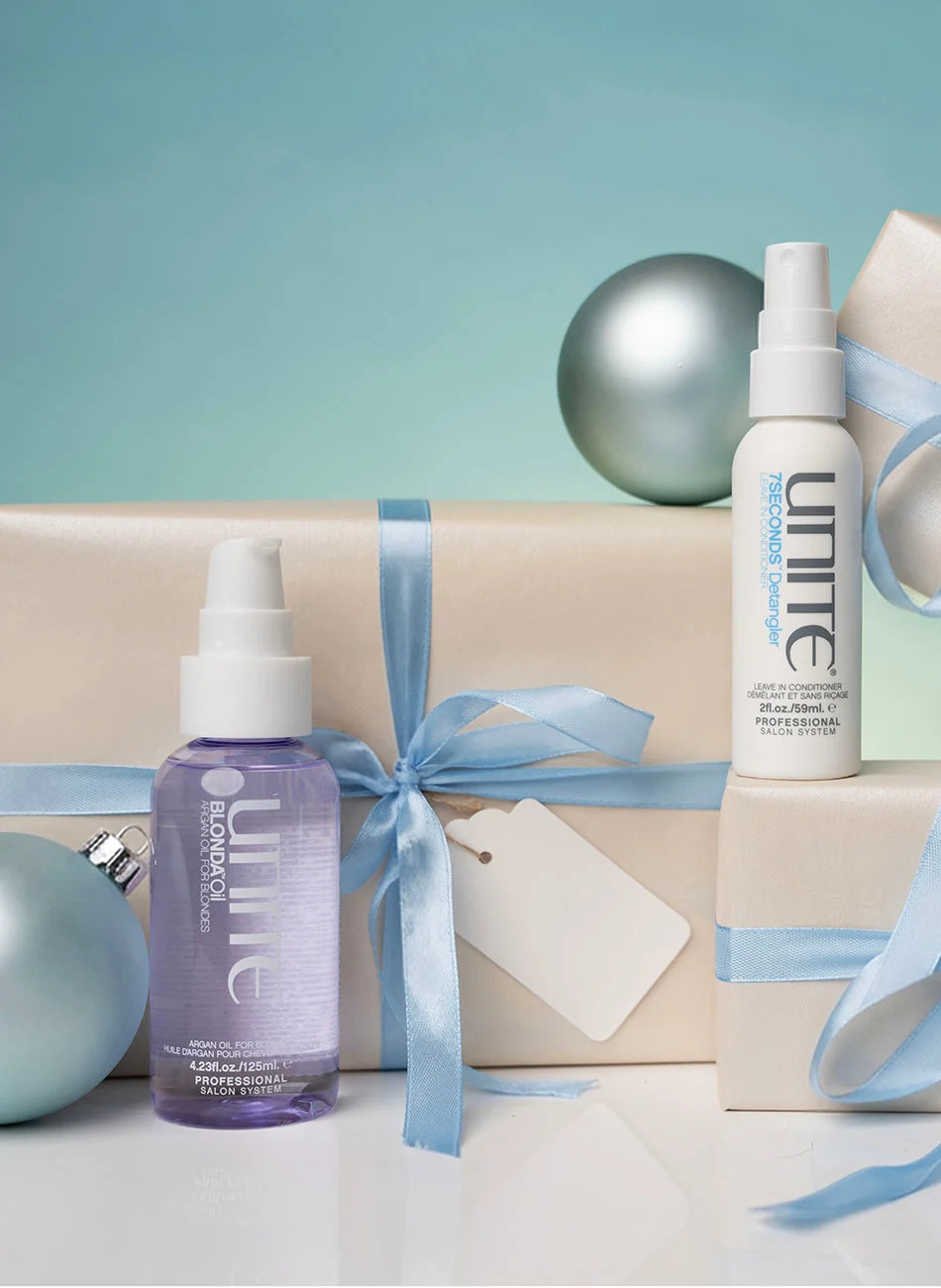 Two Umine haircare products, a purple bottle and a white spray bottle, styled on top of wrapped gift boxes with blue ribbons and decorative silver ornaments against a teal background.