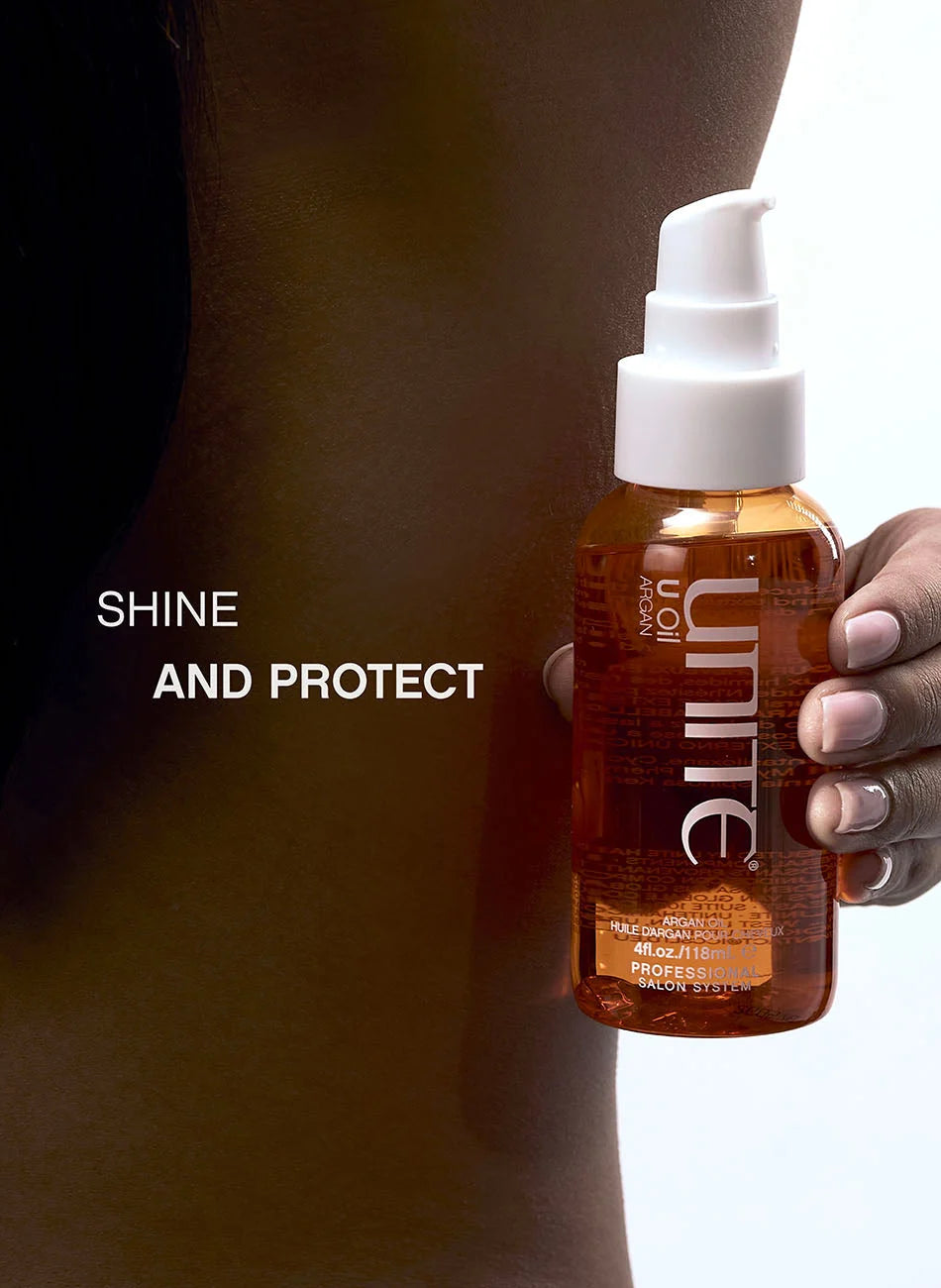 A hand holds a bottle of Unite Non-Oil Professional Shine Spray against a model's neck, with the text 'SHINE AND PROTECT' on the left. The bottle is amber brown with a white pump dispenser.