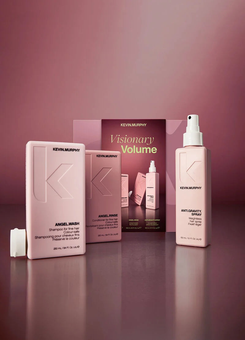 Kevin Murphy haircare set featuring a large Angel Wash bottle, a smaller Angel Hair product, and a Visionary Volume box, alongside an Antimicrobial Spray, arranged on a reflective surface against a dusty rose background.