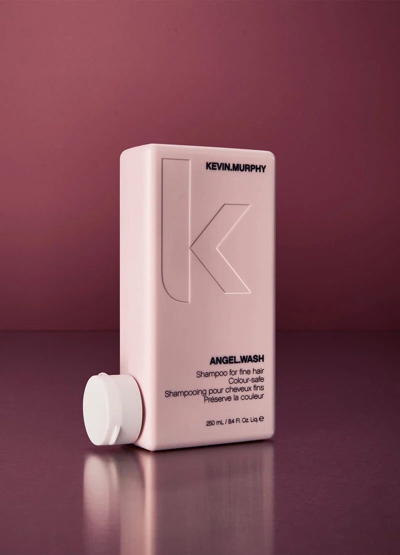 A pale pink Kevin Murphy Angelwash shampoo bottle with a matching detached white cap, set against a dark plum purple background.